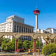 Calgary skyline with Bow Tower and historic downtown buildings framed by Eau Claire bridge with red columns and Latin inscrip